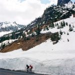 Two cyclists on roadside of snowy mountain pass