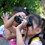 Two children birdwatching through binoculars